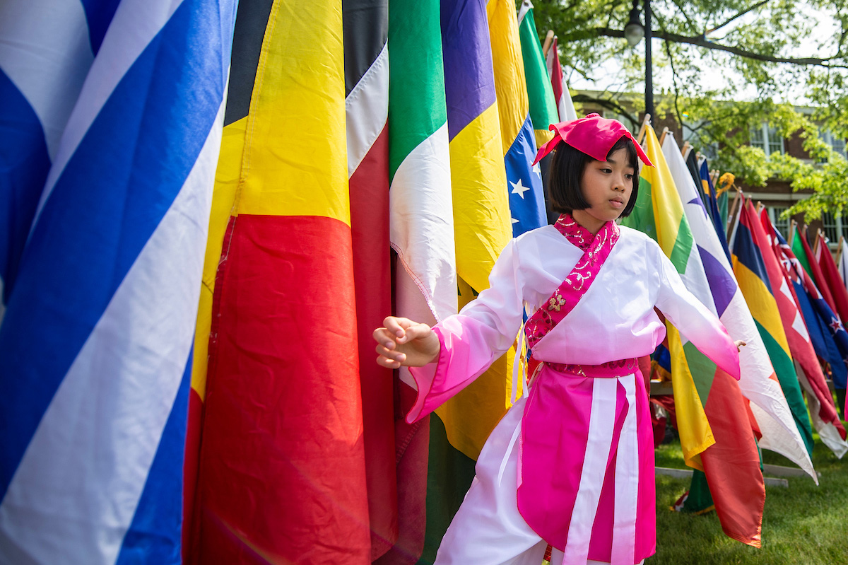 A little girl on the drill field in front of various flags from around the world