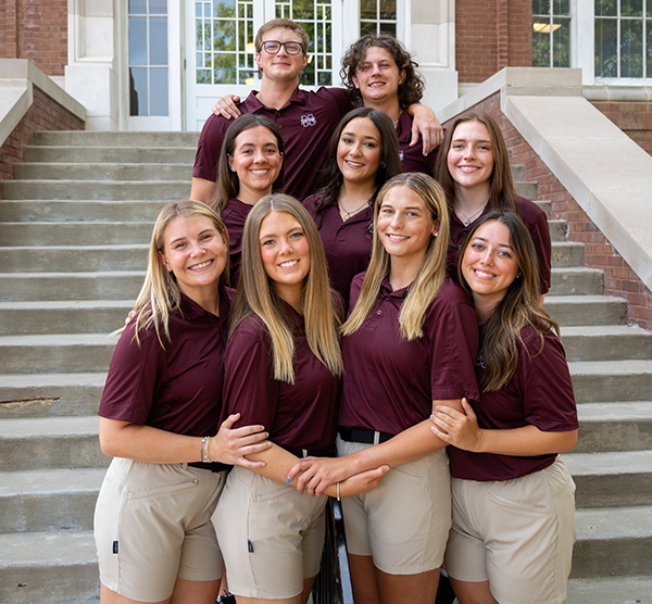 Photo of Issy Karp and eight other Orientation Leaders standing on the steps of Lee Hall at MSU.